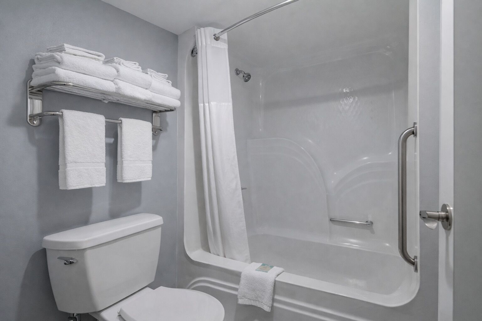 Un baño moderno con ducha envuelta en vidrio, inodoro y toallero con toallas dobladas.