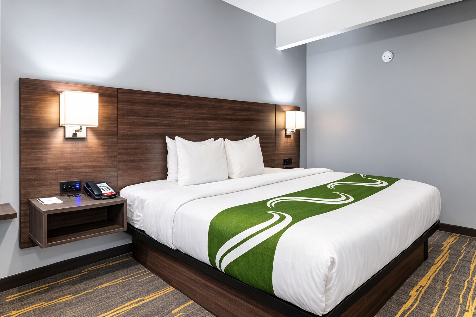 A hotel room with a large bed, two bedside tables, a phone, and a lamp.