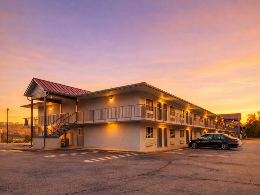 Un motel con una estructura de dos pisos, una zona de estacionamiento techada y un automóvil estacionado al frente.