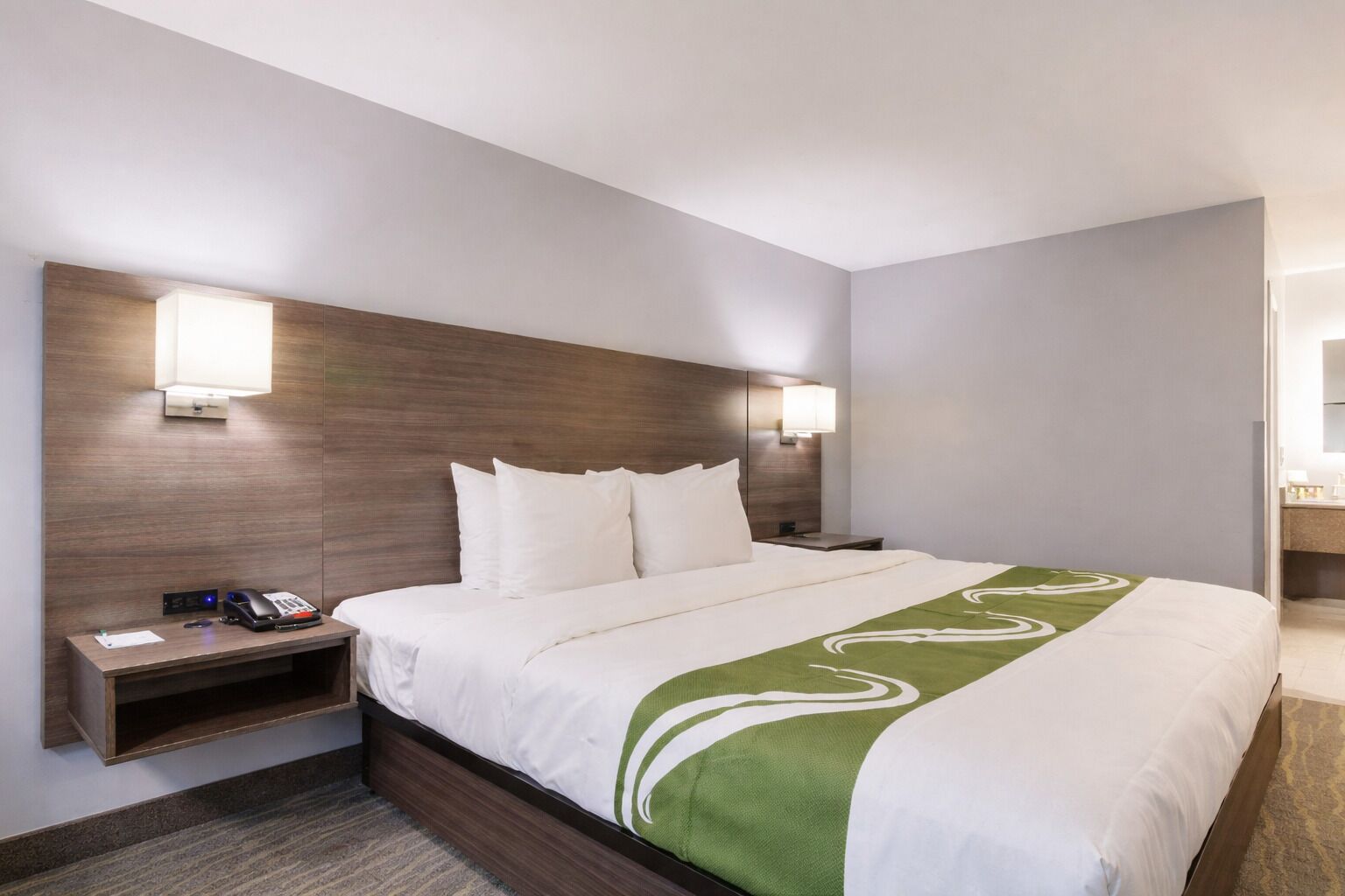 A hotel room with a large bed, bedside tables, a desk, and a mirror.