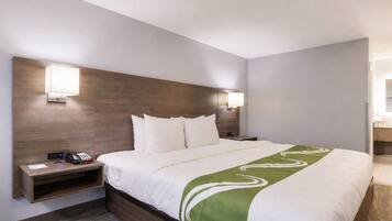 A hotel room with a large bed, bedside tables, a desk, and a mirror.