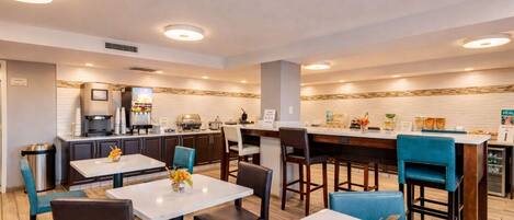 Ein moderner Hotel-Speiseraum mit mehreren Tischen, Stühlen, einer Kaffeestation und einer Theke mit Speisekarte.