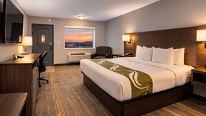 Habitació d'hotel amb un llit gran, una escriptori, una cadira, una televisió, una finestra amb vista al capvespre i una làmpada penjada a la paret.