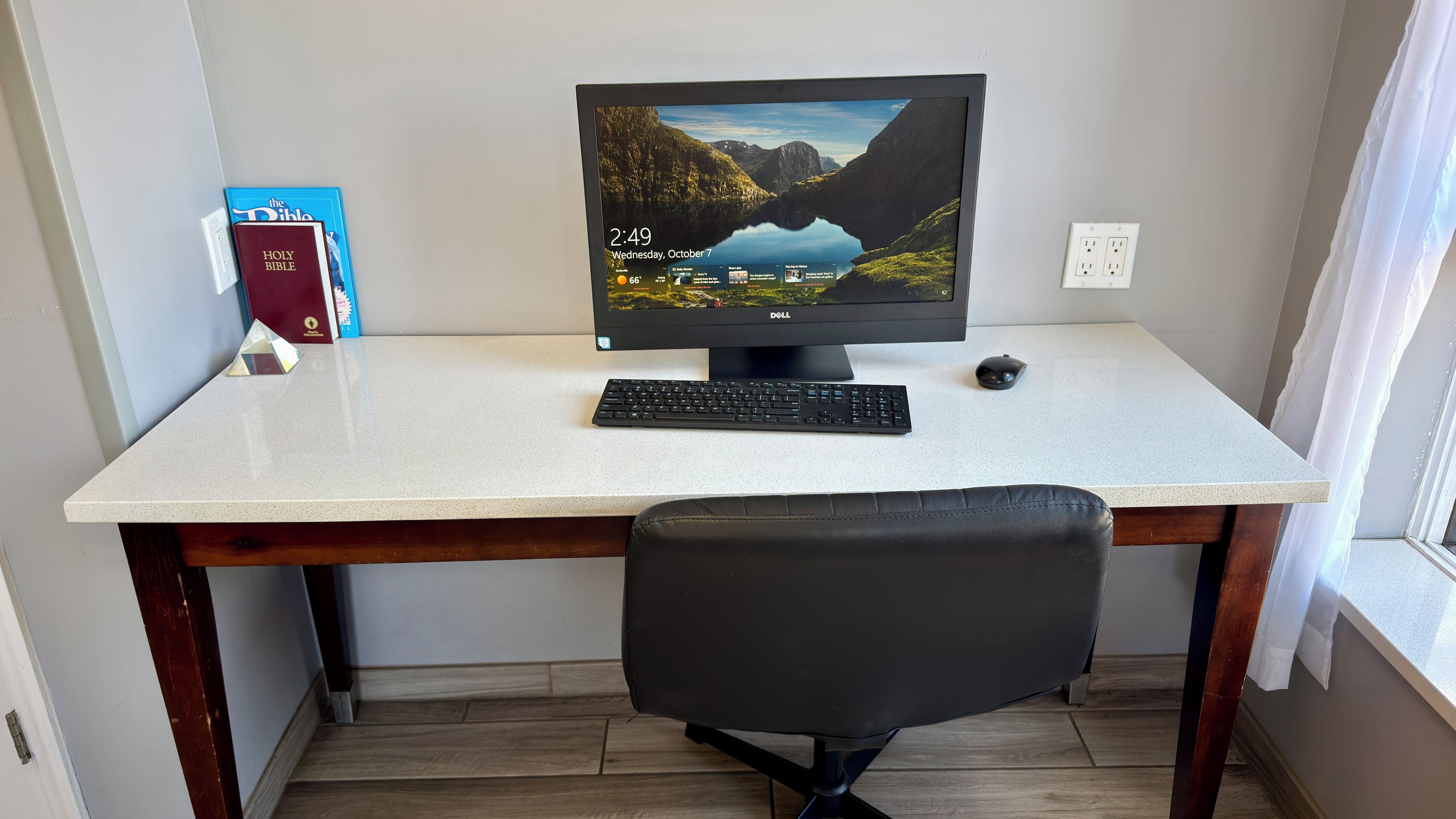A desk with a computer, keyboard, and mouse, a chair, and books on the wall.
