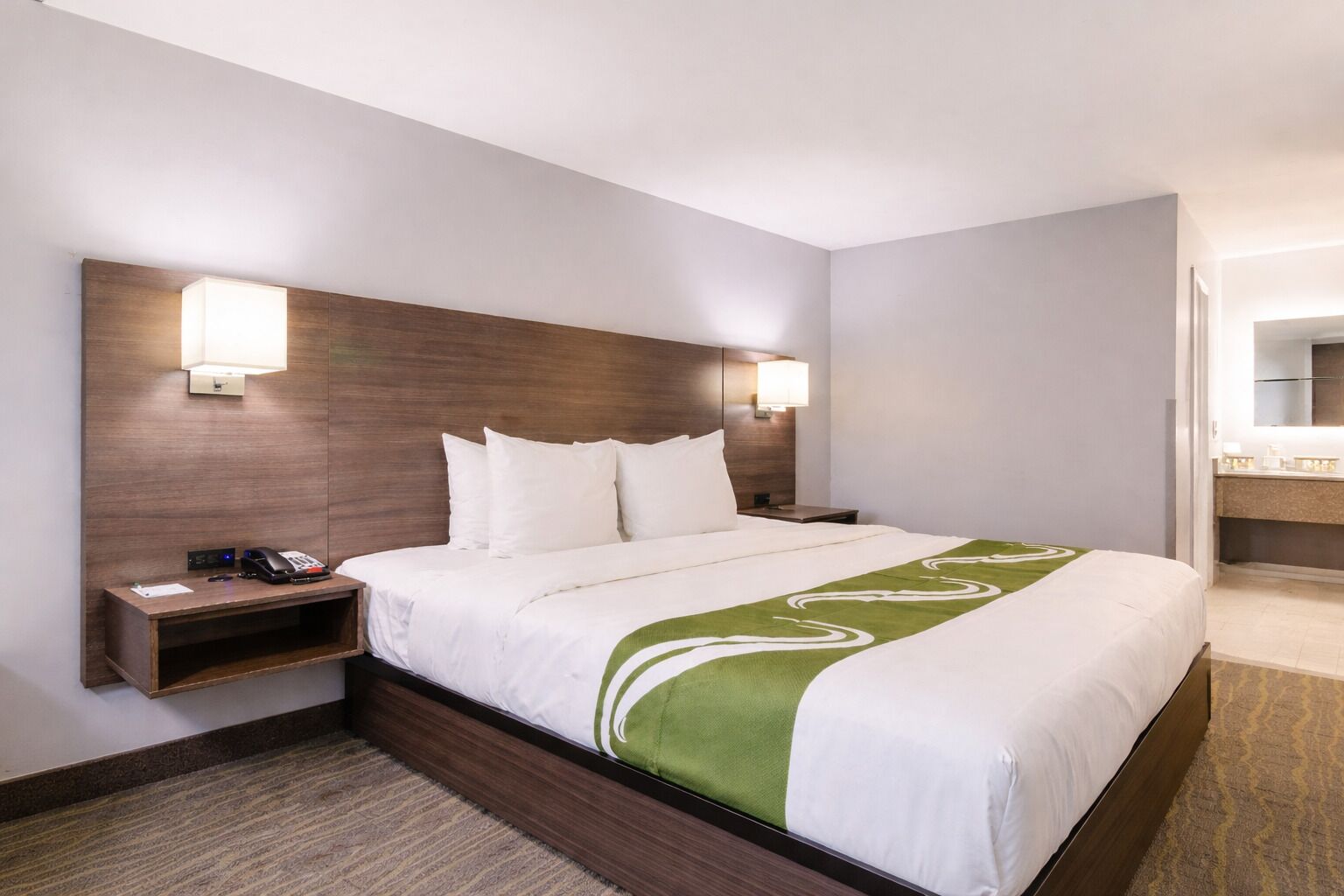 A hotel room with a large bed, a bedside table with a phone, and a nightstand.