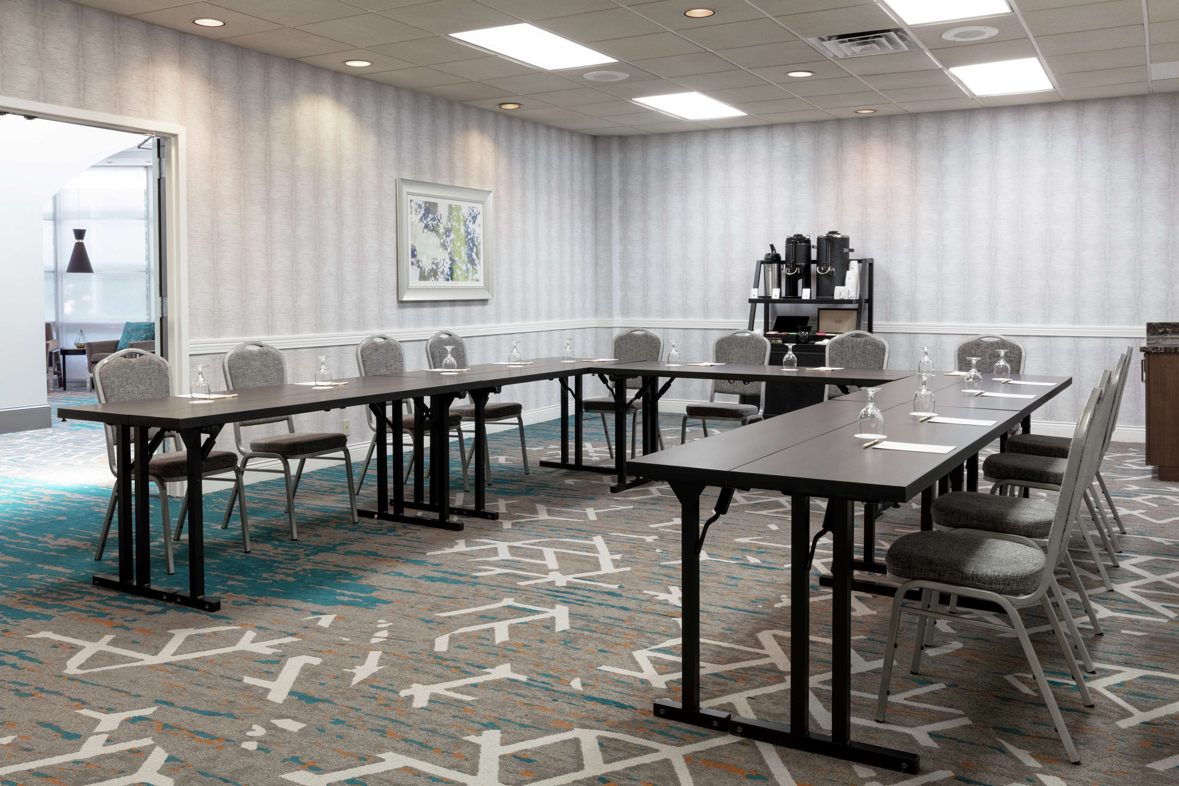 A conference room with a long table, chairs, a patterned carpet, and a bookshelf with items.