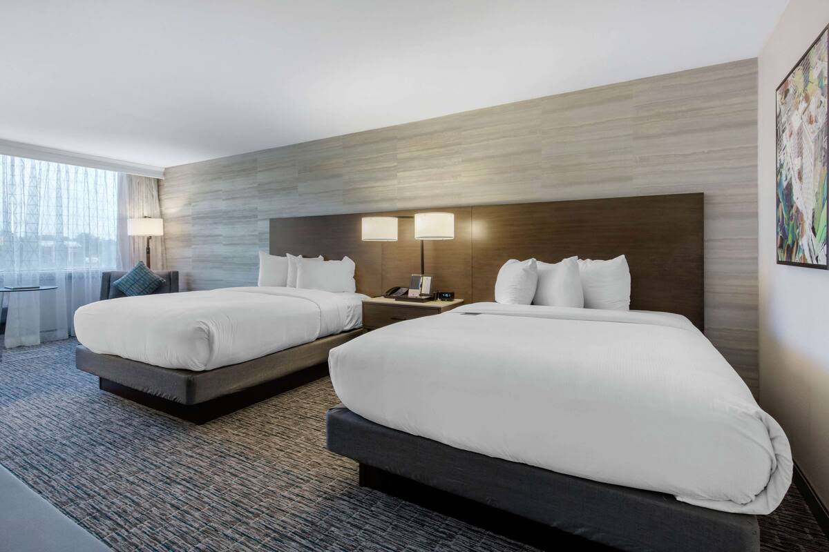 A hotel room with two beds, a desk, and a window with curtains.