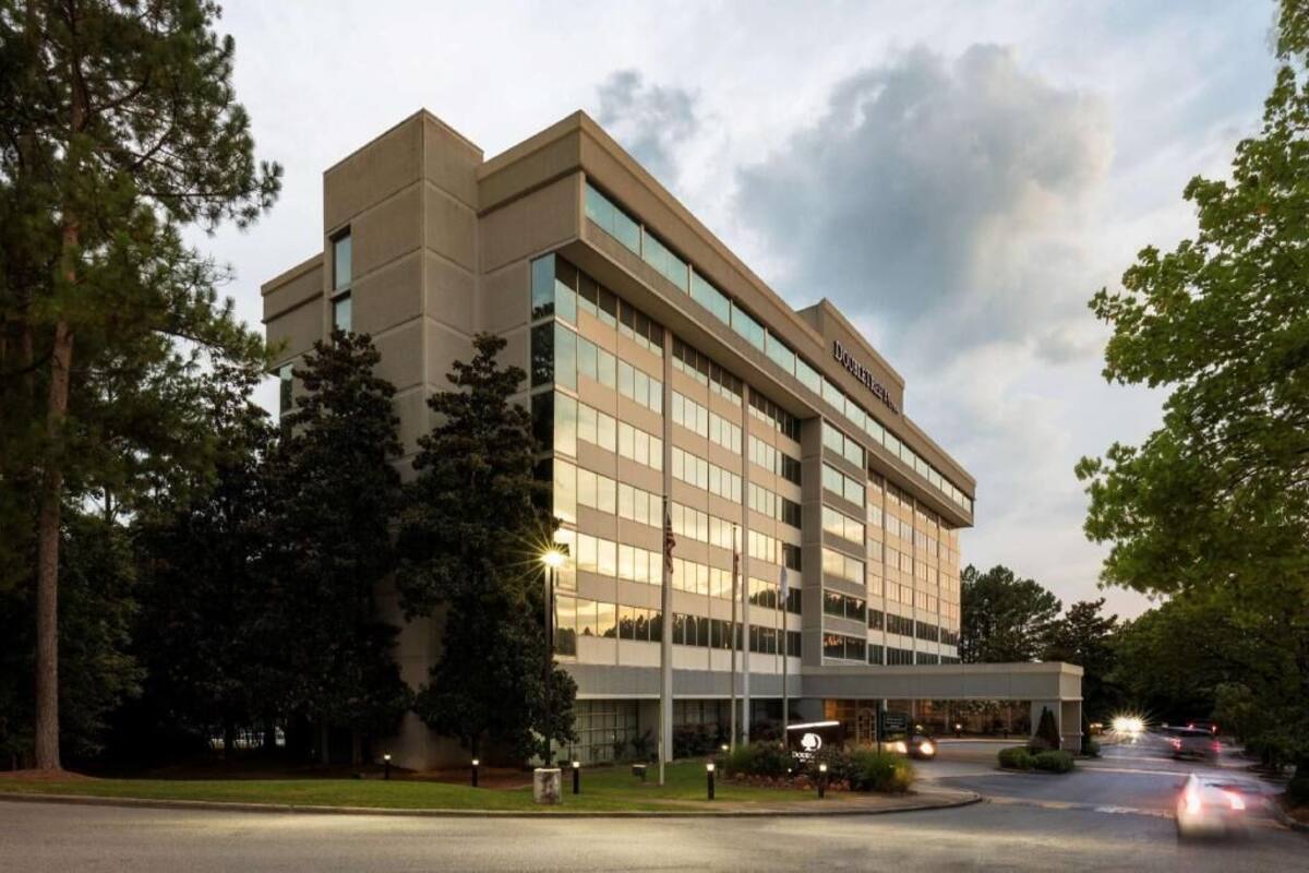 A modern hotel building with a flat roof, large windows, and a covered entrance area.