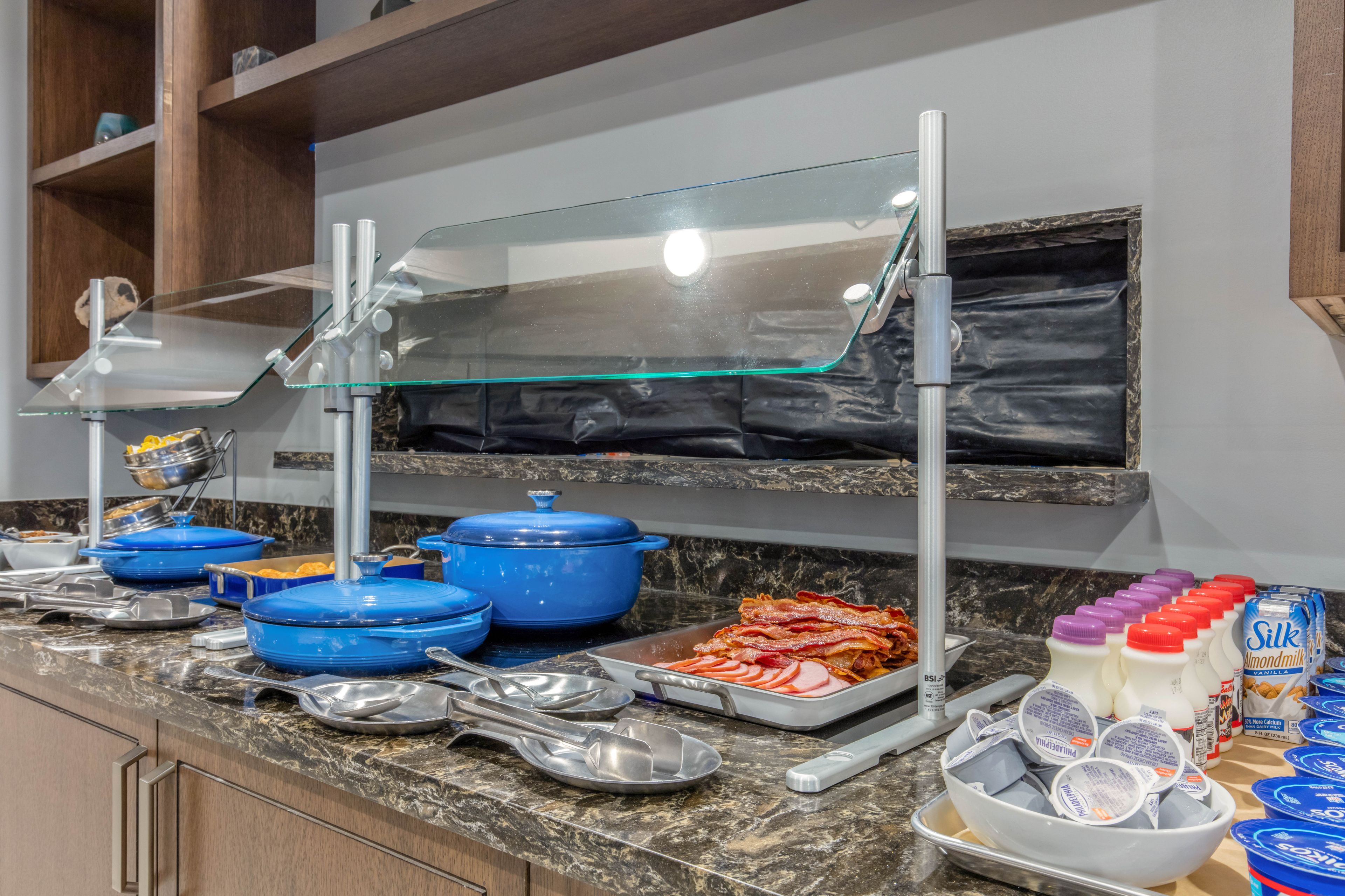 Montaje tipo bufé con fuentes azules, una estación de servicio cubierta con vidrio y diferentes opciones de comida, como tocino y cartones de leche.