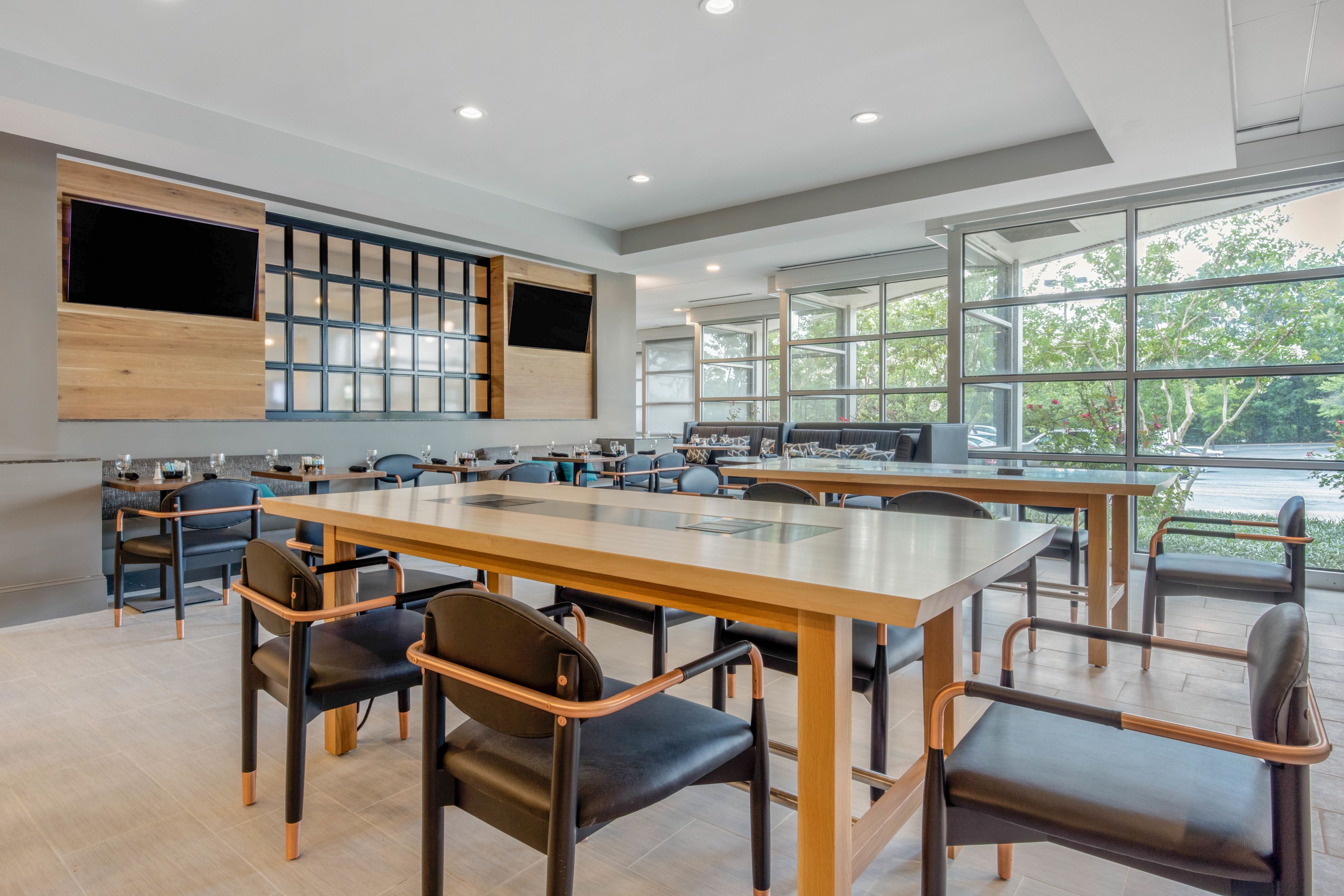 A modern conference room with large tables and chairs, a wooden accent wall, and large windows offering a view of trees.
