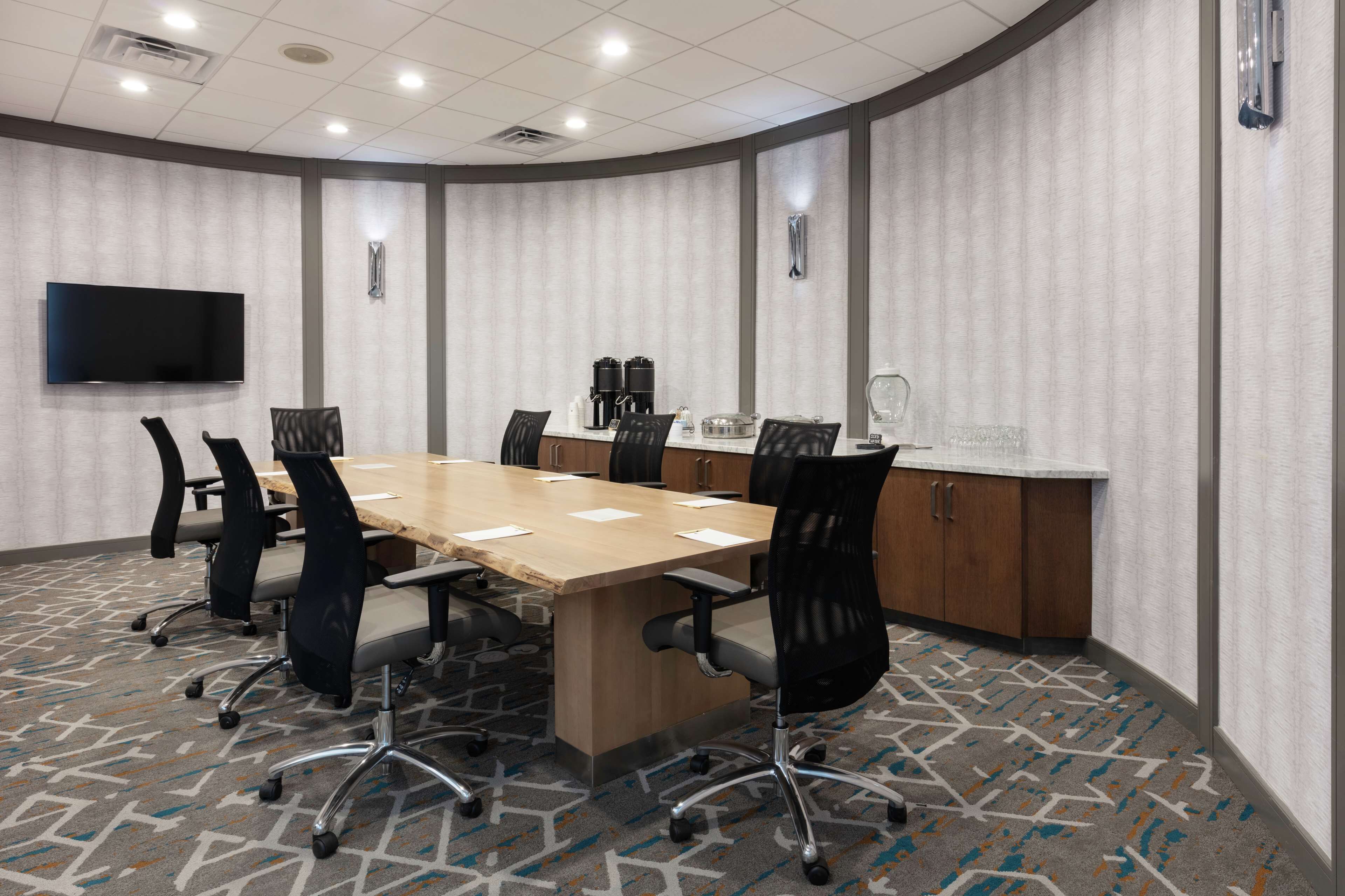 A conference room with a long table, multiple chairs, a flat-screen TV, and a coffee station.