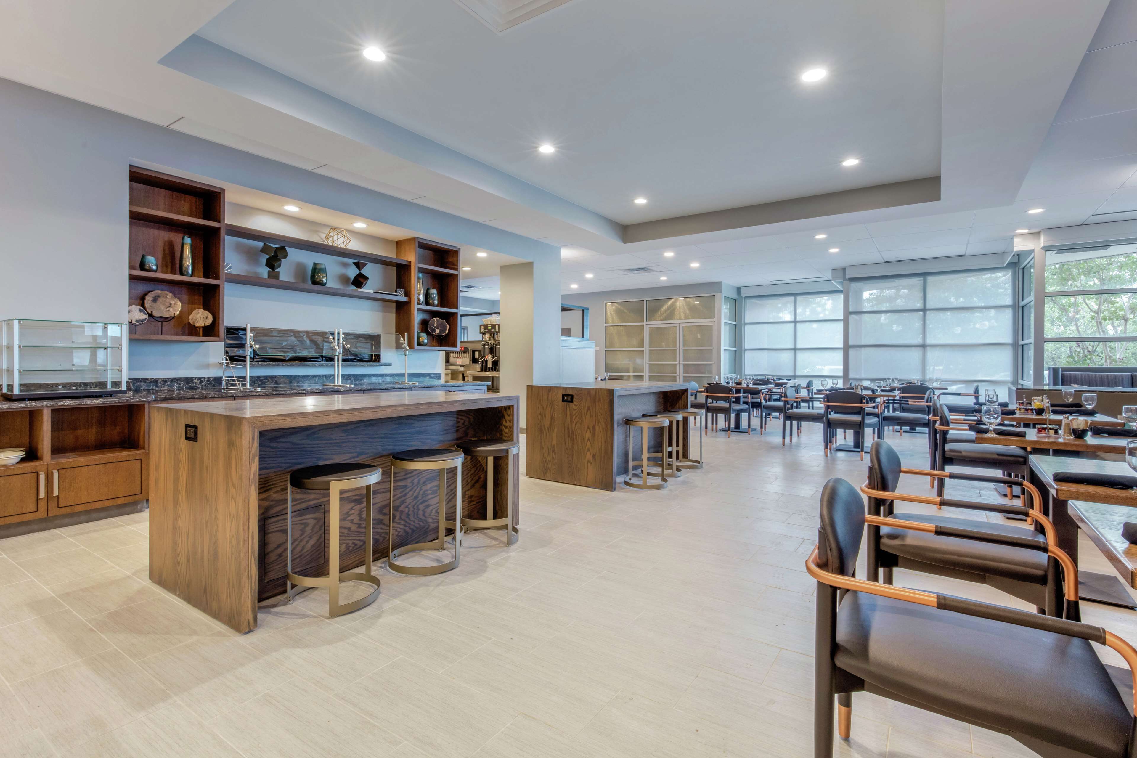A spacious restaurant with a central bar area, multiple seating options, and large windows providing natural light.