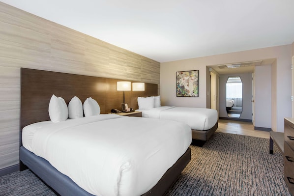 Habitación de hotel con dos camas, cabeceros, lámparas de noche, mesitas de noche, un espejo y piso alfombrado.