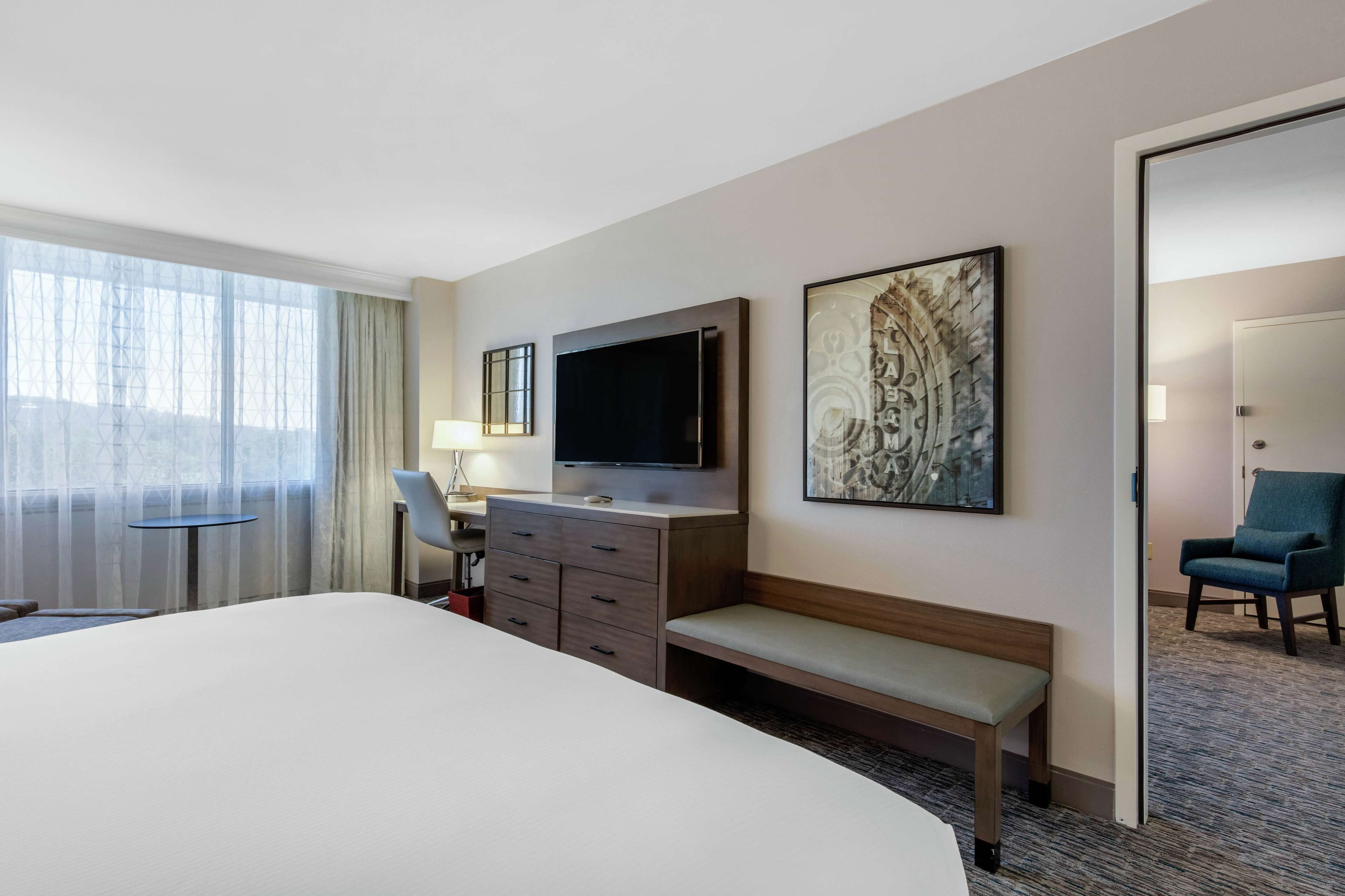 A hotel room with a large bed, a desk with a chair, a television, and artwork on the wall.