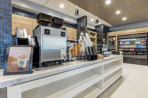 A modern coffee shop interior with a coffee machine, a beverage dispenser, and a refrigerated beverage display. - DoubleTree by Hilton Birmingham Perimeter Park (Birmingham)