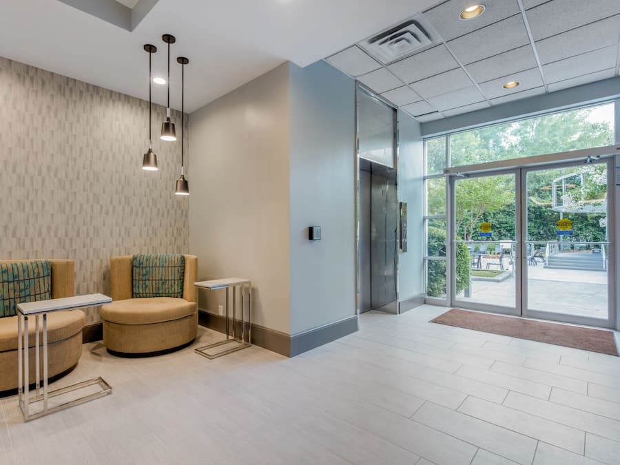 A modern lobby with two cushioned seating areas, a reception desk, and a large glass door leading outside.