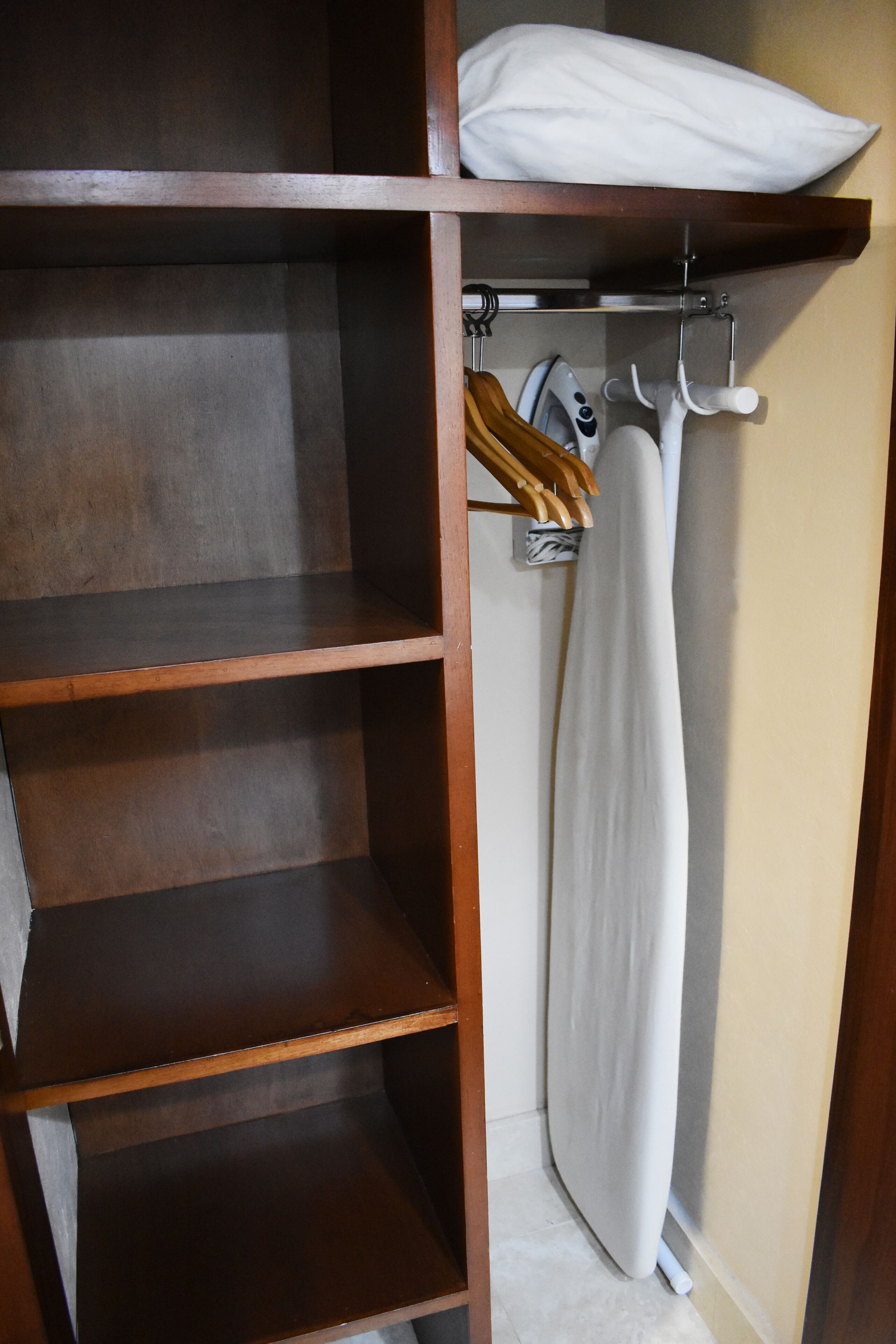 Un armario de madera con estantes, una barra para colgar ropa y una tabla de planchar.