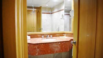 Un baño con lavamanos de mármol, un espejo y una ducha.