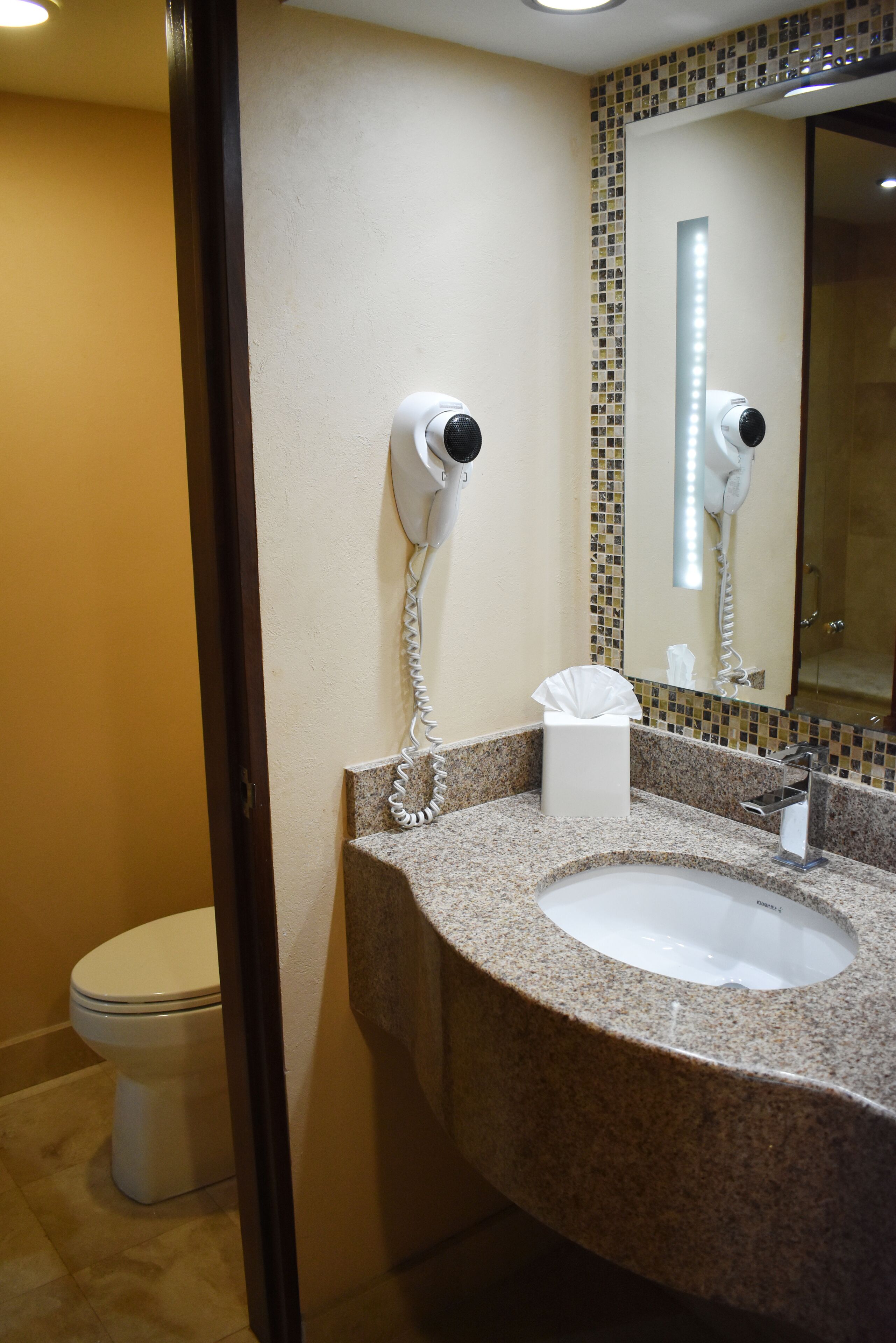 A bathroom with a granite countertop, a white sink, a hairdryer, and a toilet.