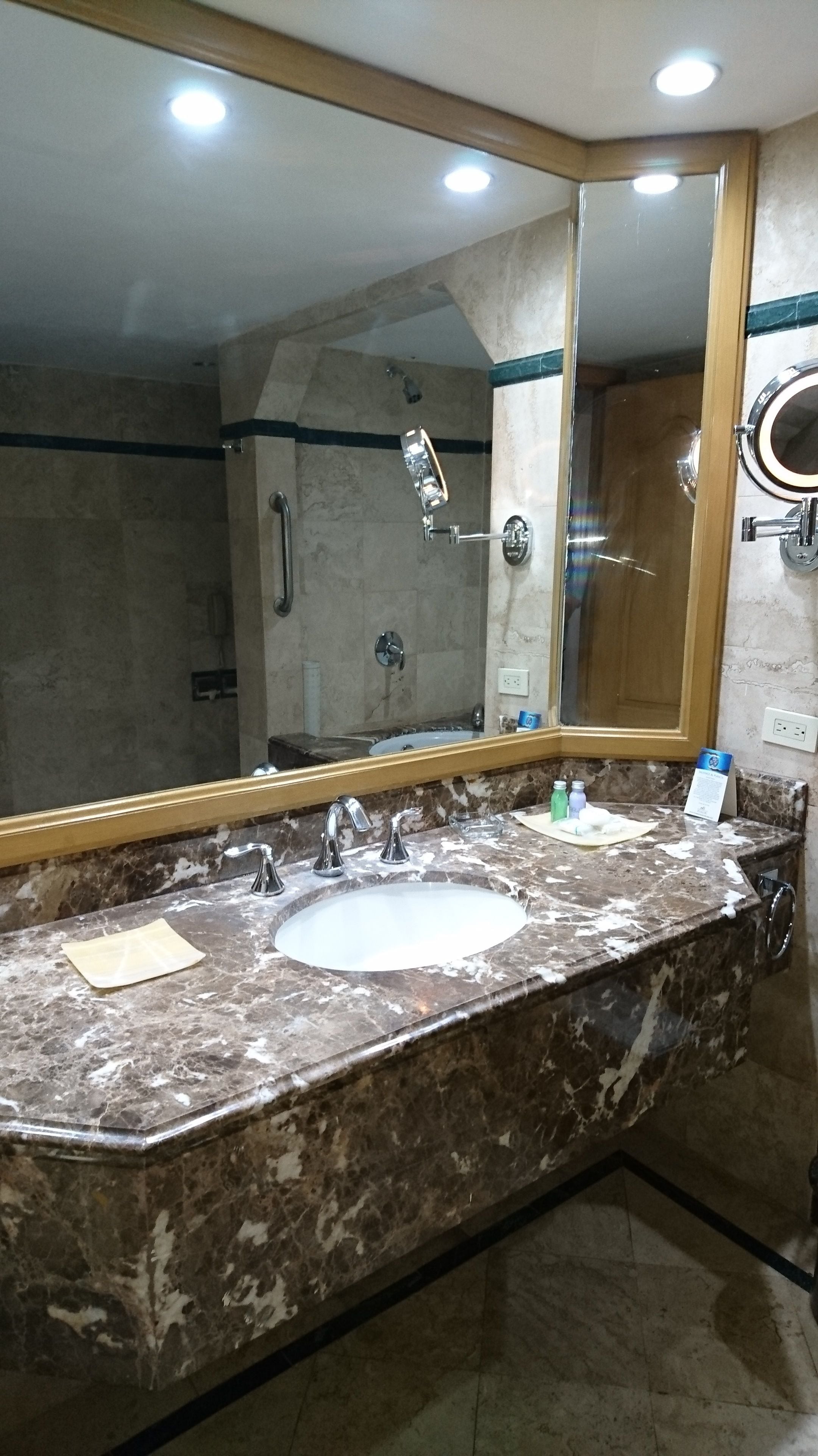 Un baño con lavamanos de mármol, un espejo grande y una zona de ducha.