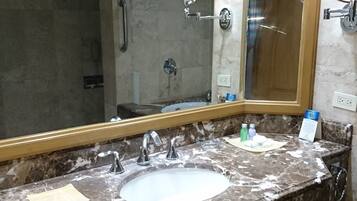 Un baño con lavamanos de mármol, un espejo grande y una zona de ducha.