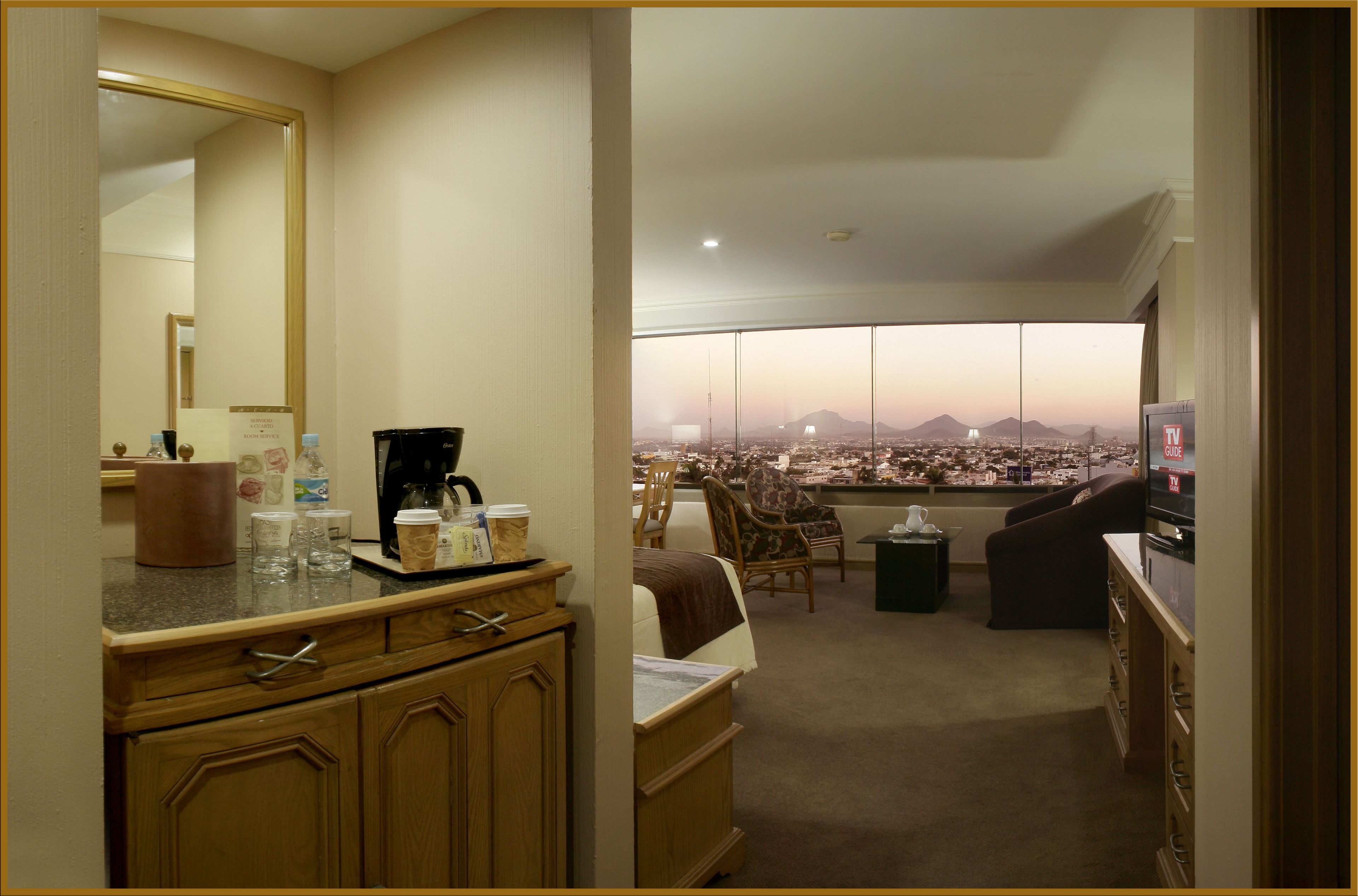 Ein Hotelzimmer mit Küchenzeile, einem großen Spiegel, einem Fernseher und Blick auf eine Stadtlandschaft mit Bergen.