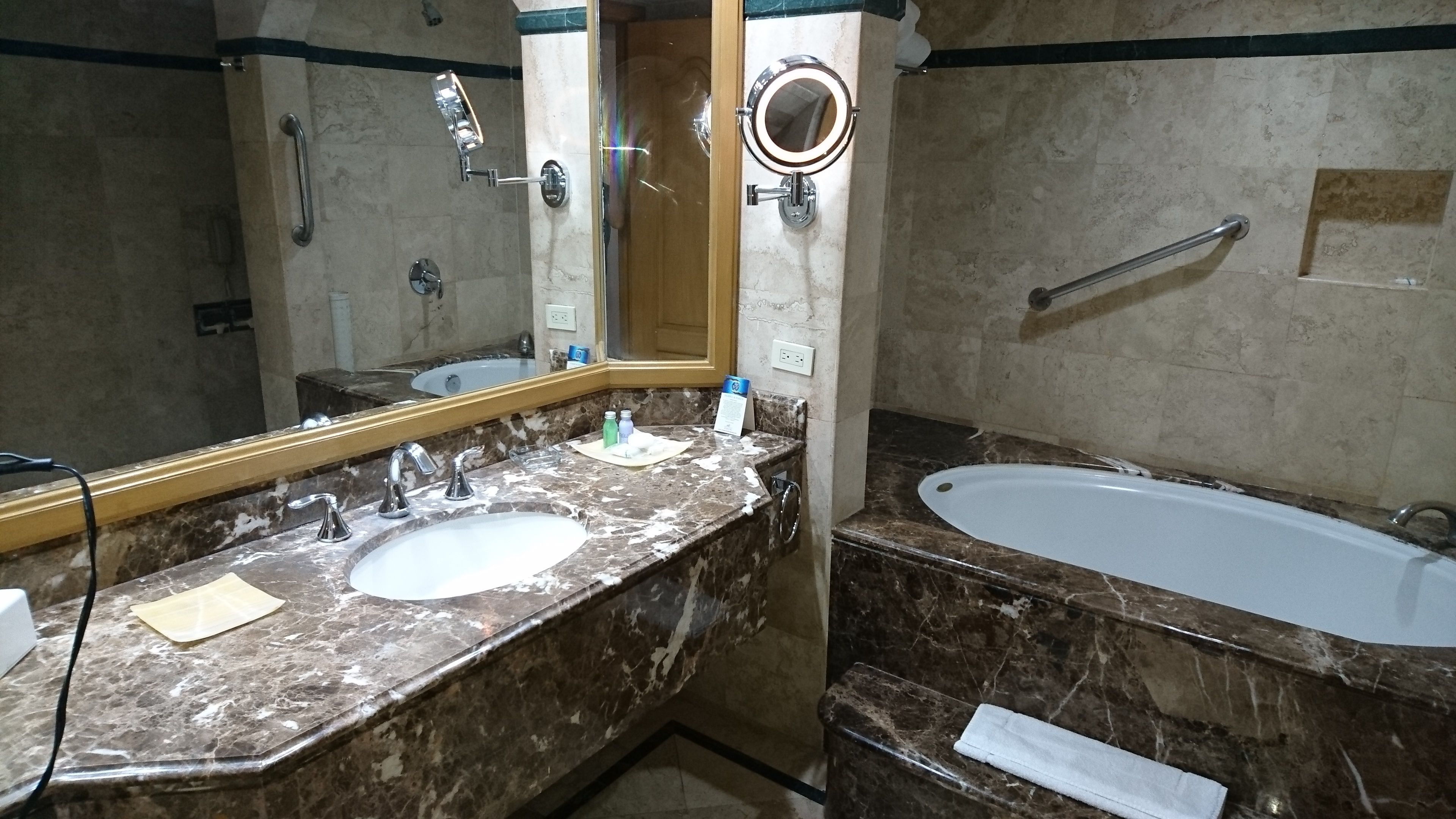 Un baño con tocador de mármol, un lavabo, un espejo, cabezal de ducha de mano y bañera.
