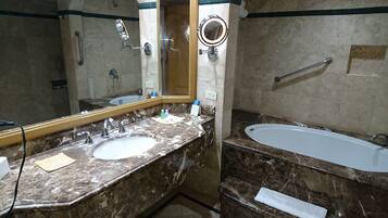 Un baño con tocador de mármol, un lavabo, un espejo, cabezal de ducha de mano y bañera.