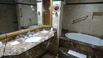 Un baño con tocador de mármol, un lavabo, un espejo, cabezal de ducha de mano y bañera.