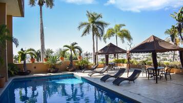 Relax by the rooftop pool with a stunning city view, surrounded by lush greenery and comfortable lounge seating.