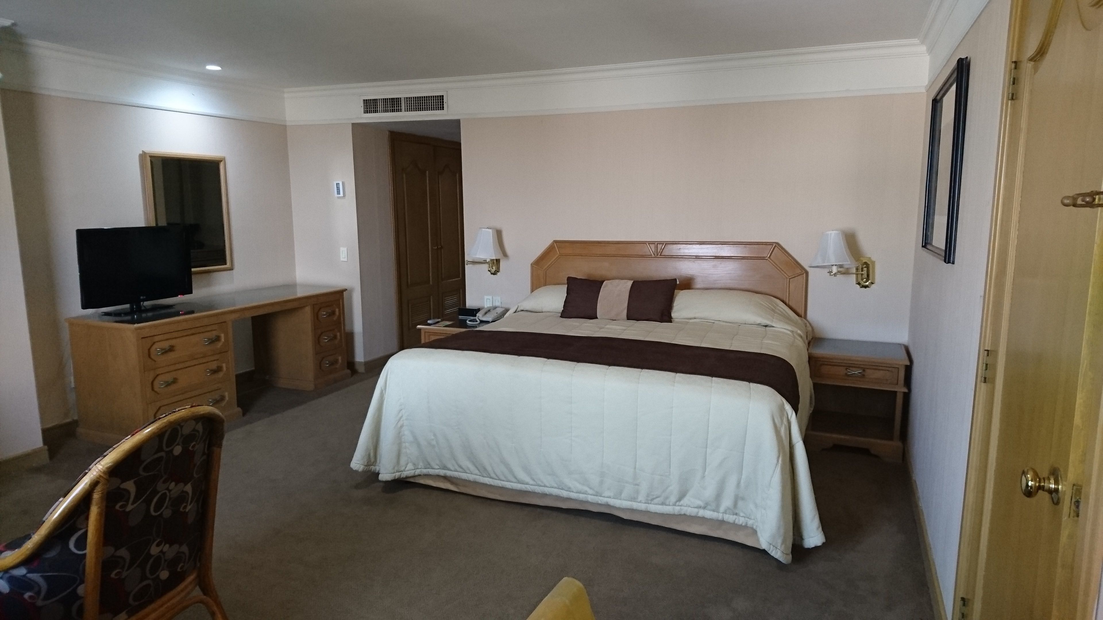 A hotel room with a bed, a desk with a television, a chair, and a door.