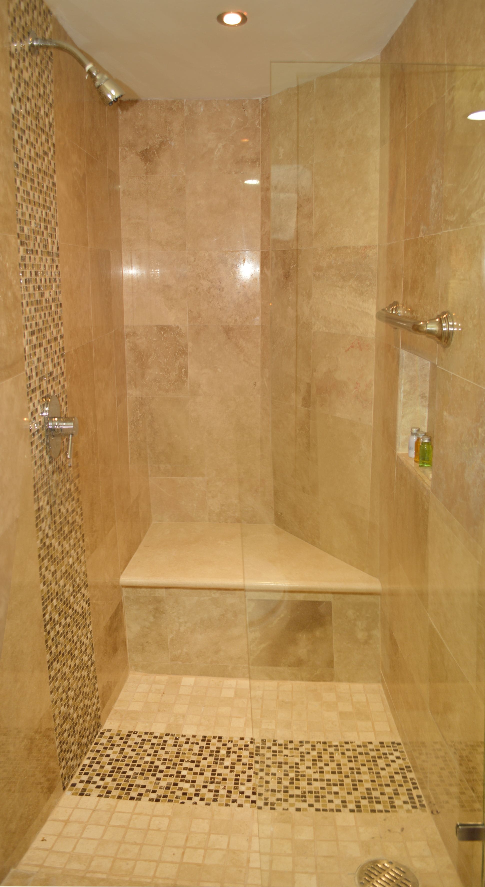 Eine bodenebene Dusche mit Glastür, gefliesten Wänden und einer Sitzbank.