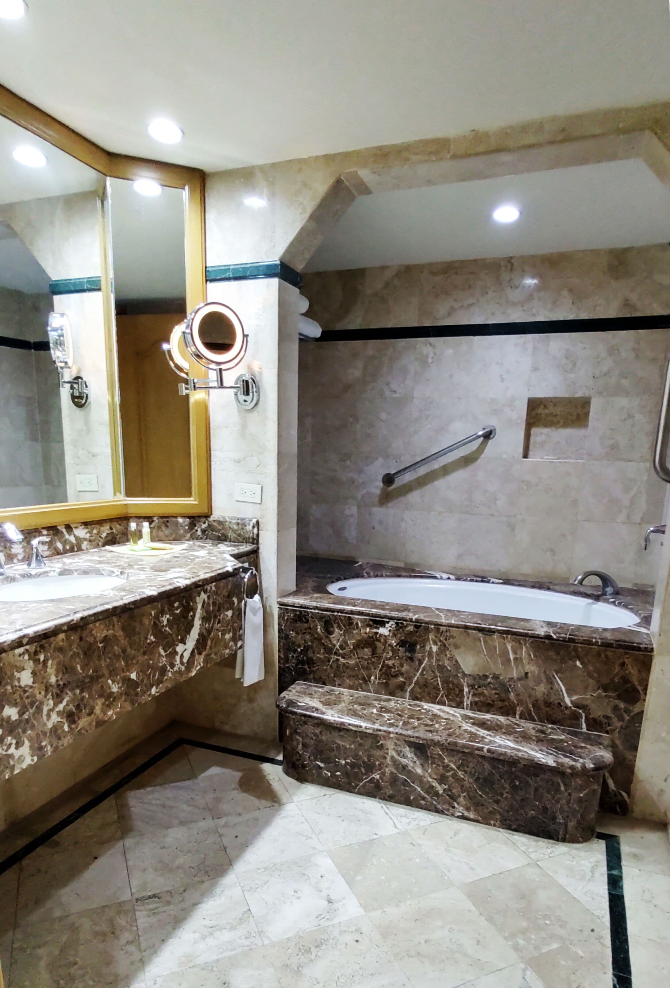 A bathroom with a marble sink, a large mirror, a bathtub, and a shower area.