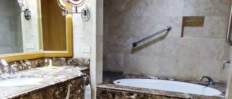 A bathroom with a marble sink, a large mirror, a bathtub, and a shower area.