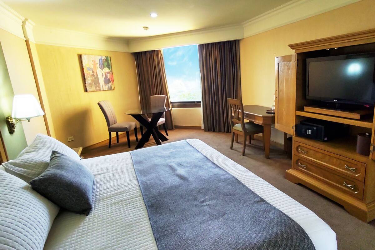 Een hotelkamer met een groot bed, een televisie, een bureau en een stoel.
