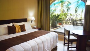 Quarto de hotel com uma cama grande, uma escrivaninha e vista para palmeiras pela janela.