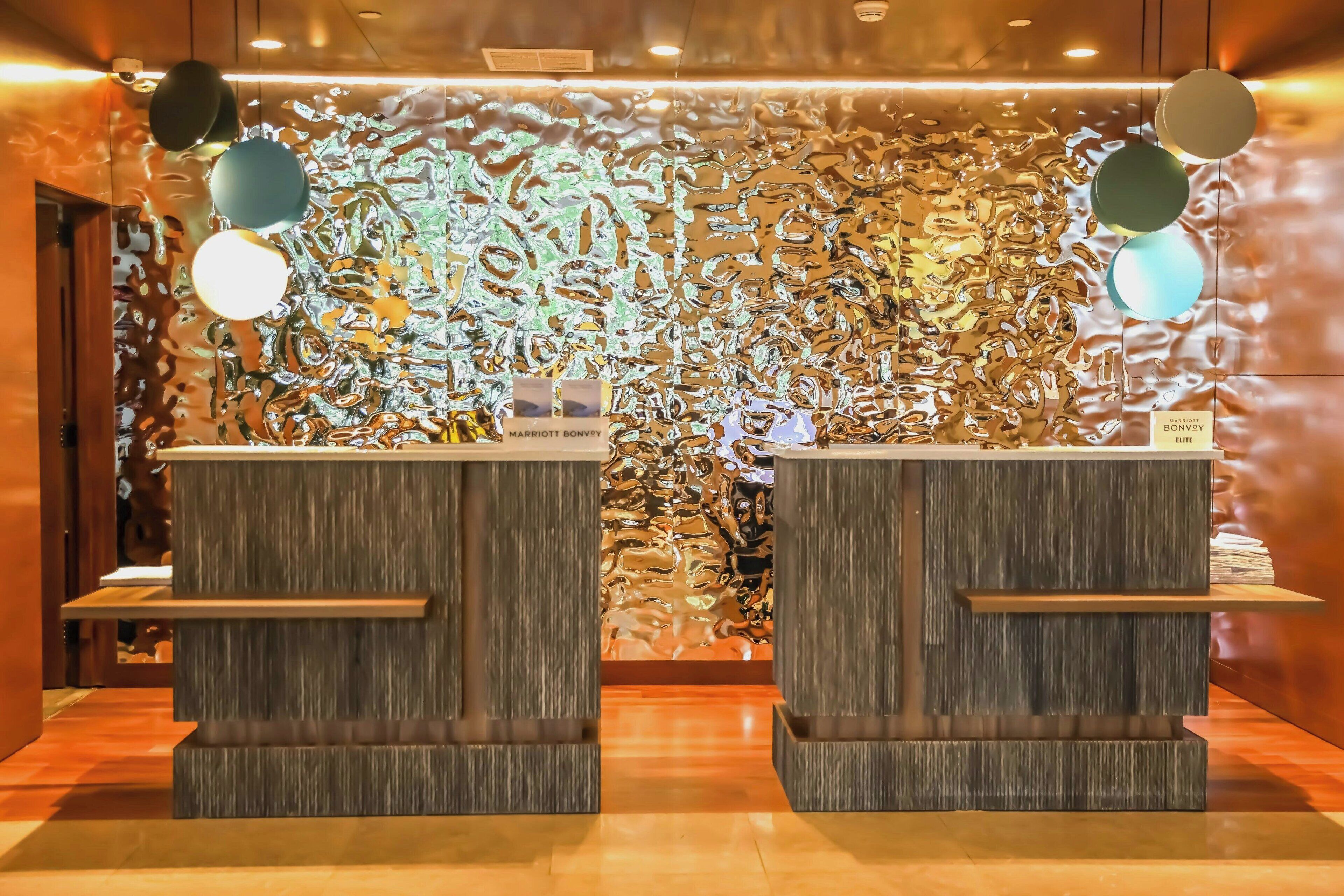 A reception area with two wooden reception desks, a textured wall with abstract patterns, and hanging spherical lights.