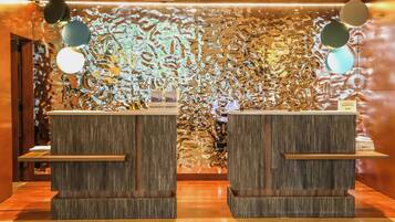 A reception area with two wooden reception desks, a textured wall with abstract patterns, and hanging spherical lights.