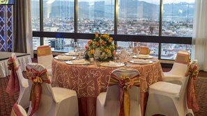 A round table set for a meal with chairs, a floral centerpiece, and a city view through large windows. - Delta Hotels by Marriott San Jose Aurola (San José)