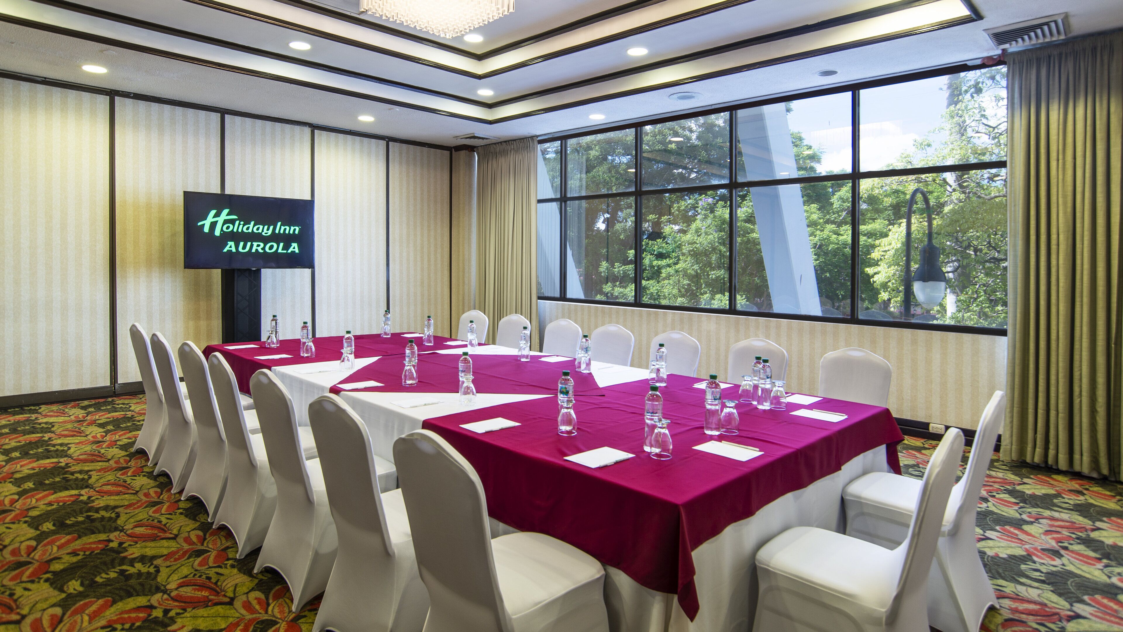 A conference room with tables set for meetings, white chairs, and a large window with a view of trees.