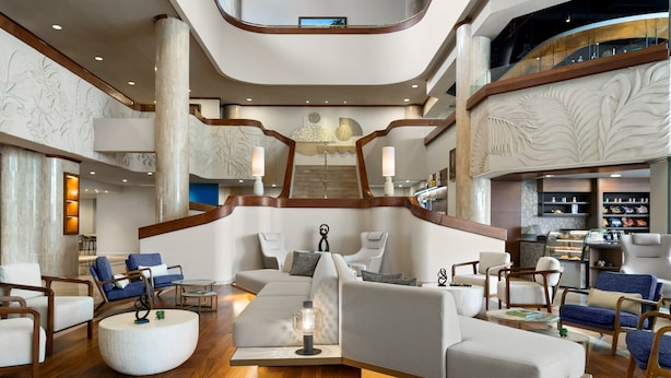 Un hall d’entrée spacieux avec un escalier central, des coins salon et une cuisine ouverte.