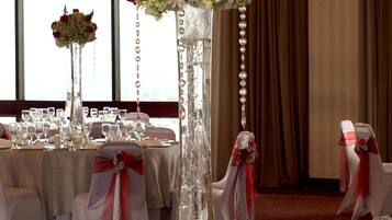 A banquet hall with round tables set for a formal event, featuring tall floral centerpieces and elegant table settings.