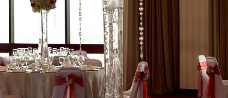A banquet hall with round tables set for a formal event, featuring tall floral centerpieces and elegant table settings.