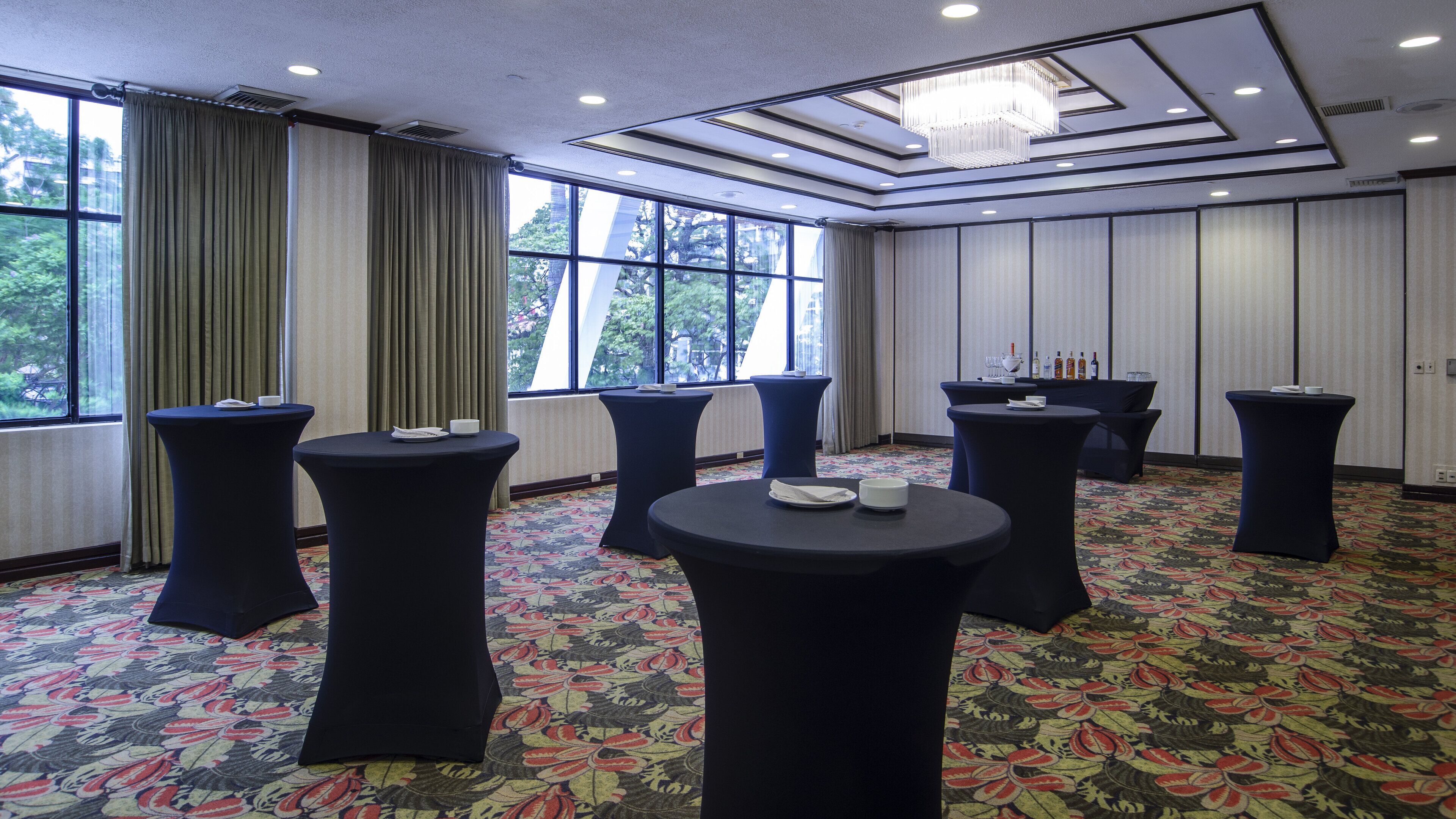 A conference room with round tables, a chandelier, and large windows with curtains.