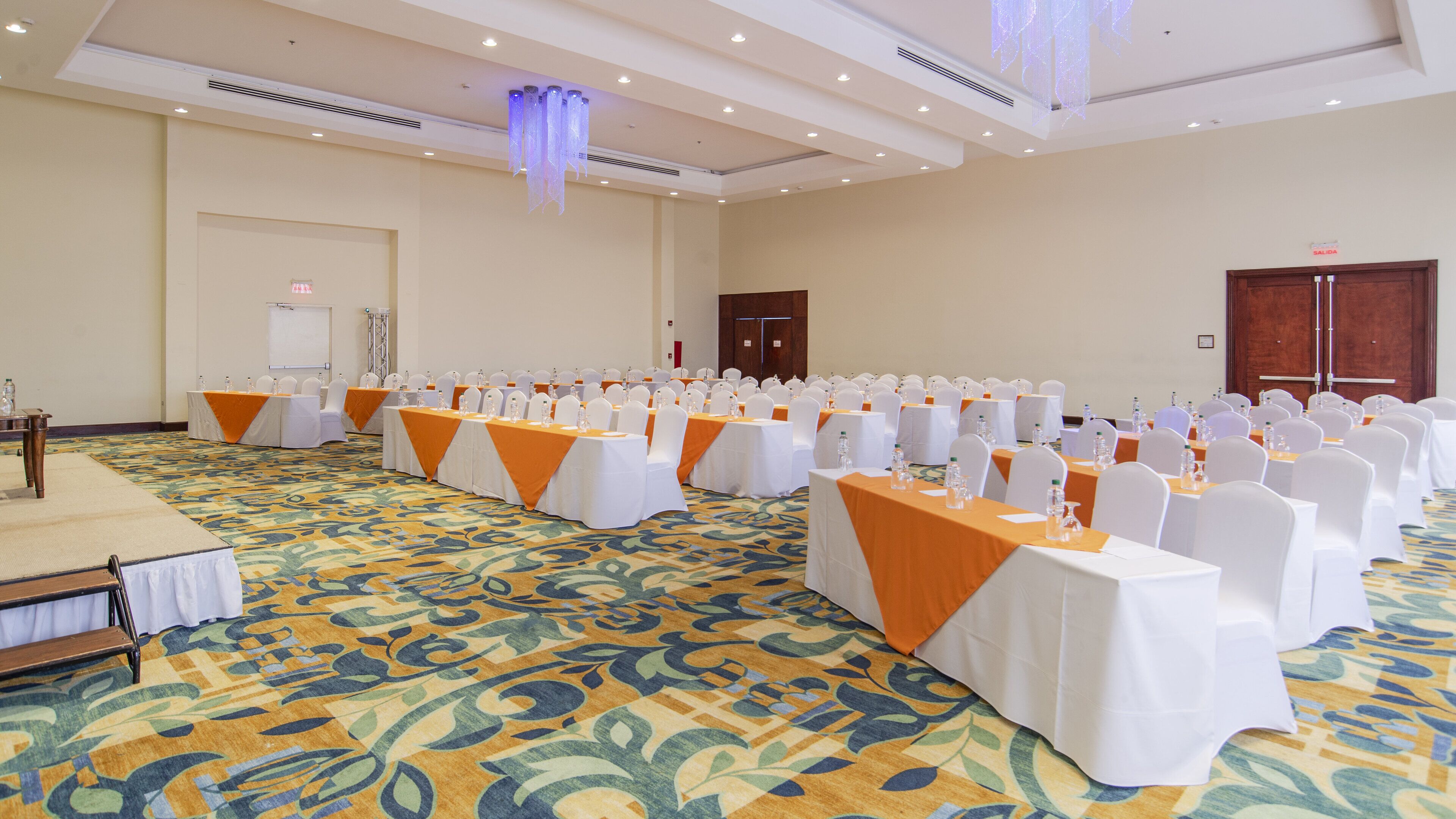 Un salón de conferencias con filas de mesas, sillas blancas y manteles naranjas.