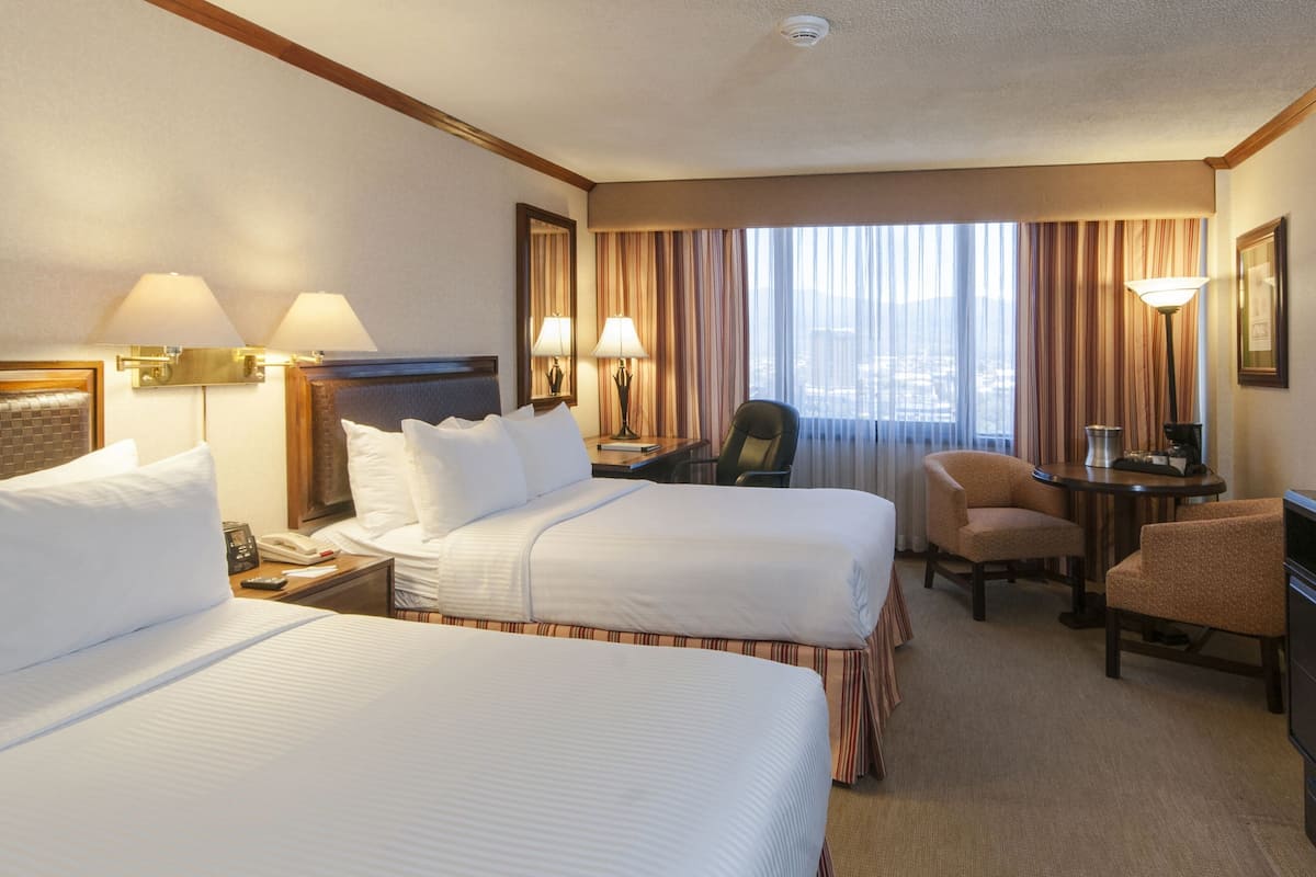 A hotel room with two beds, a desk, a chair, and a large window with curtains.