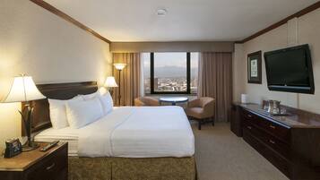 A hotel room with a large bed, two bedside lamps, a desk with a TV, a small table, and a chair.