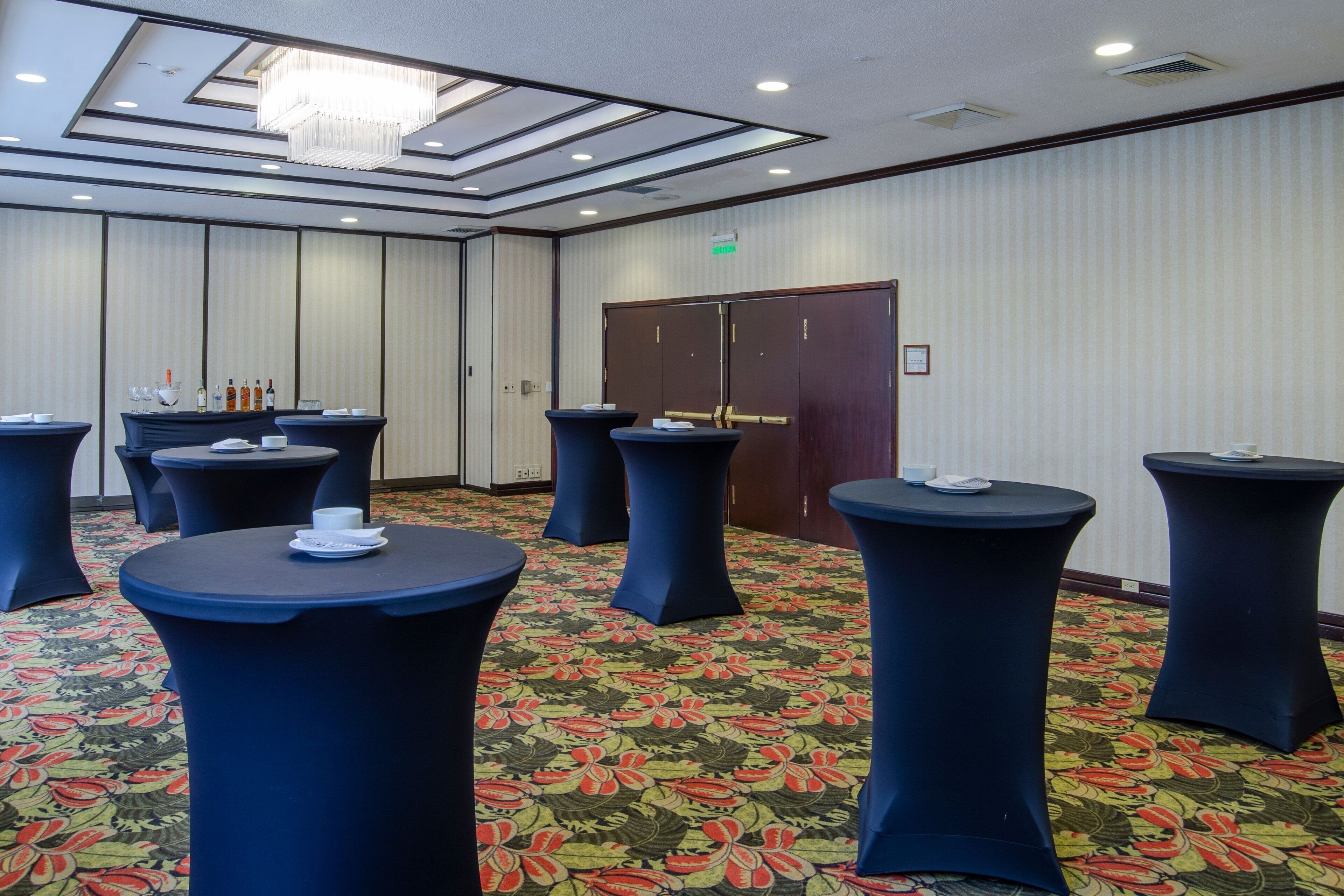 Uma sala de conferências com mesas redondas, um candelabro e um tapete estampado.