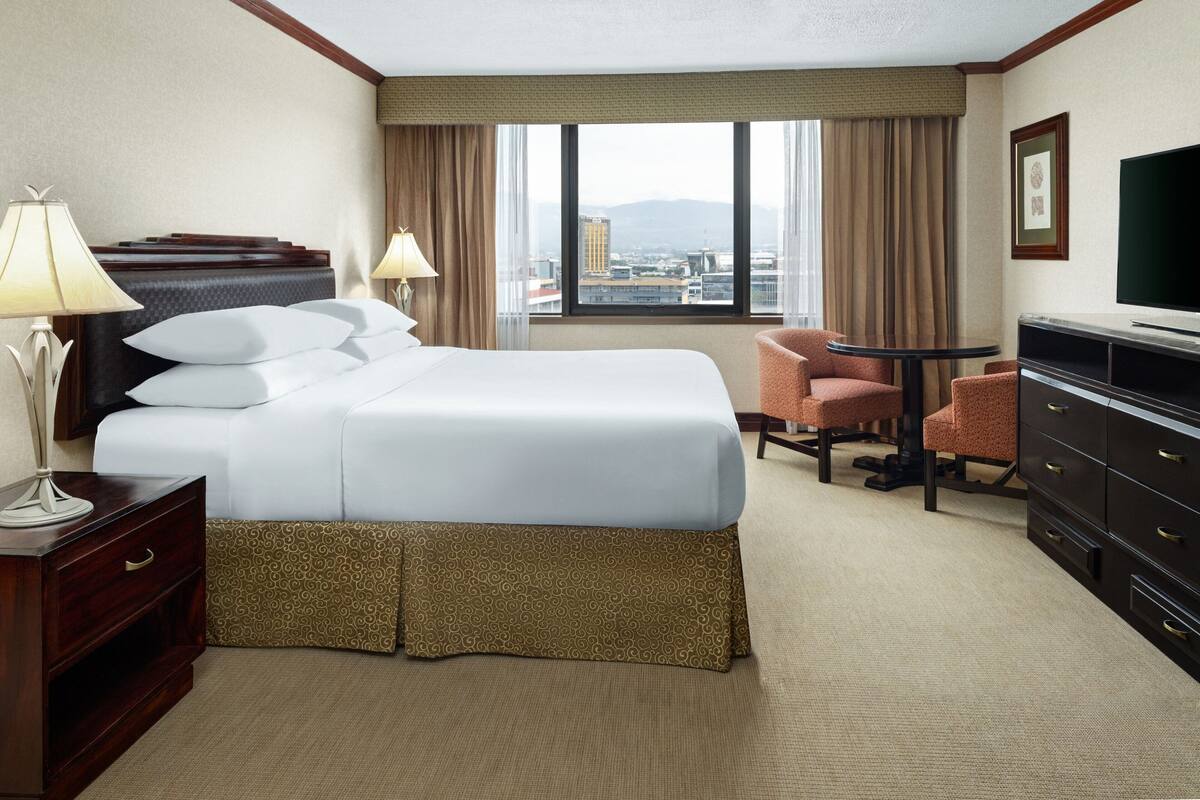 A hotel room with a large bed, two bedside lamps, a TV, a desk, and a chair.