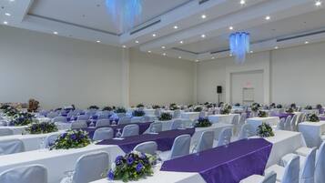Un salón de conferencias con filas de mesas, cada una cubierta con un mantel blanco y caminos de mesa morados.
